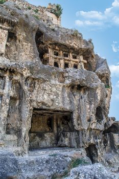 View of abandoned and destroyed rock tombs of Tlos Ancient City, on cloudy blue sky background.