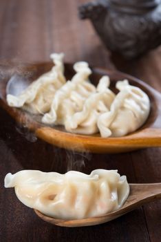 Fresh dumplings with hot steams on wood spoon. Famous Chinese food on rustic old vintage wooden background. 
