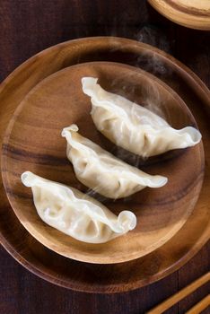 Top view fresh dumplings with hot steams on wood plate. Chinese food on rustic old vintage wooden background. 