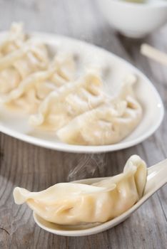 Fresh dumpling on spoon with hot steams. Chinese food on old wooden background. 