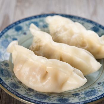 Close up fresh dumpling on plate. Chinese cuisine on old wooden background. Fractal on the plate is generic print.