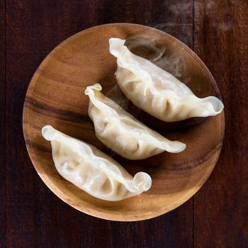 Top view close up fresh dumplings with hot steams on wood plate. Chinese food on rustic old vintage wooden background. 