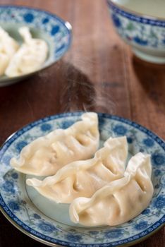 Fresh dumpling on plate. Chinese cuisine on rustic vintage wooden background. Fractal on the plate is generic print.