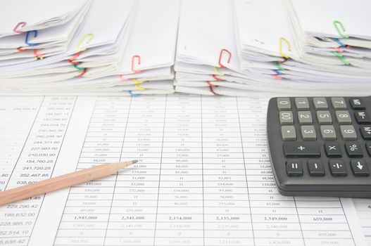 Brown pencil with calculator on finance account have step overload of old paperwork as background.