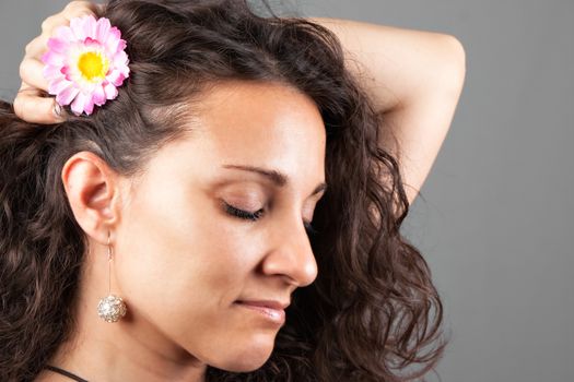 Woman with pink flower in her hair on grey background