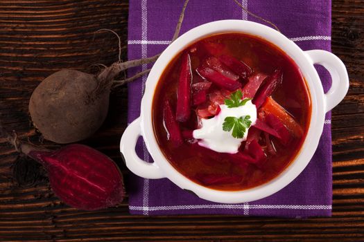 Delicious ukrainian borsch soup with fresh beetroot vegetable on purple cloth on rustic wooden table, top view. Traditional european cuisine.