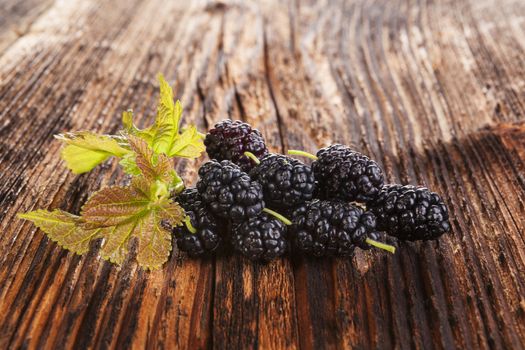 Mulberry fruit with leaves on brown wooden vintage background. Healthy summer fruit eating. Morus fruit.