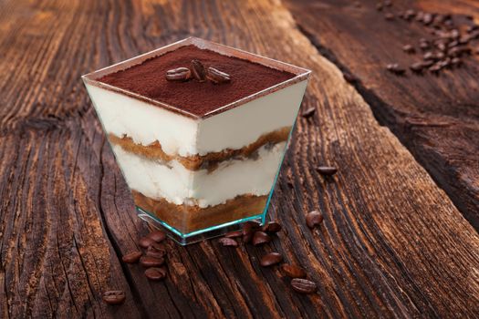 Tiramisu dessert with coffee beans on wooden textured table. Traditional tiramisu dessert, rustic, country style.