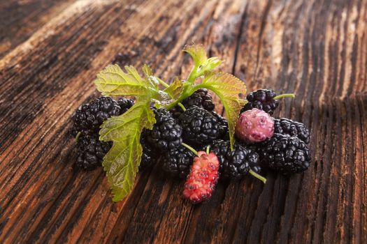 Mulberry fruit with leaves on brown wooden vintage background. Healthy summer fruit eating. Morus fruit.