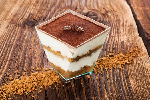 Tiramisu dessert with coffee beans and instant coffee on wooden textured table. Traditional tiramisu dessert, rustic, country style.