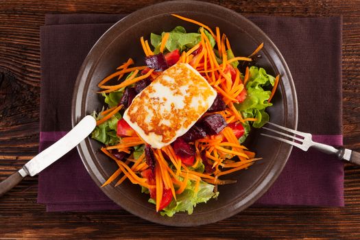 Grilled halloumi cheese with colorful fresh salad on plate on wooden table, top view. Culinary delicious vegetarian eating, mediterranean style.