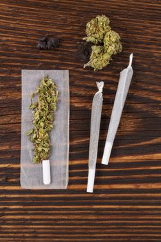 Marijuana abuse. Cannabis bud, joints, rolling paper on wooden textured background. 