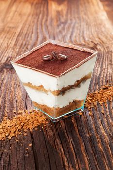 Tiramisu dessert with coffee beans and instant coffee on wooden textured table. Traditional tiramisu dessert, rustic, country style.