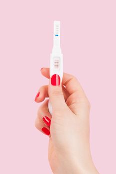 Beautiful female hand with red fingernails holding positive pregnancy test isolated on pink background. Motherhood, pregnancy, birth control concept. Minimal sparse modern image language. 