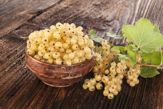 Ripe white currant in wooden bowl on old vintage wooden background. Healthy summer fruit eating. 