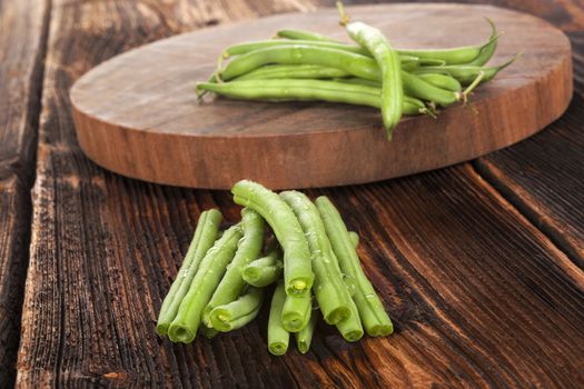 Fresh green beans with water drops on brown wooden textured table. Fresh vegetable eating. 