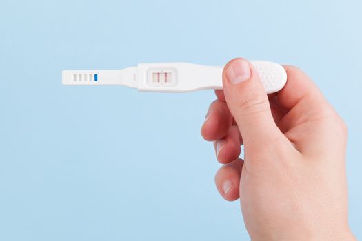 Male hand holding positive pregnancy test isolated on light blue background. Happy father.