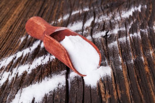 Baking soda on wooden spoon on brown wooden textured background.