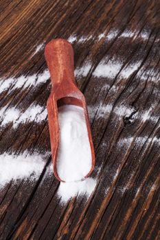 Baking soda on wooden spoon on brown wooden textured background.