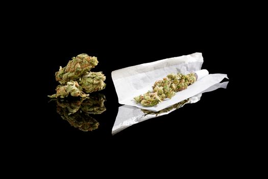 Marijuana bud and cigarette rolling paper isolated on black background. Smoking cannabis, addiction or medical use.