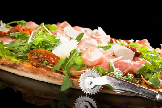 Delicious pizza with prosciutto ham, sundried tomatoes and fresh herbs. Culinary pizza eating. 
