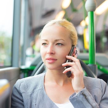 Blonde caucasian business woman talking on cell phone, traveling by bus. Public transport and commuting to work.