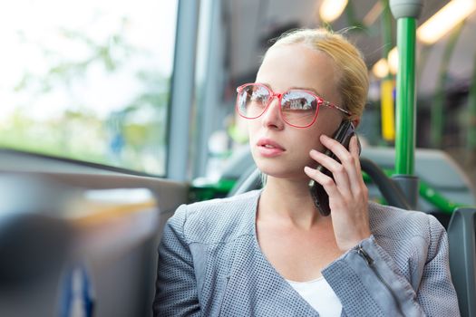 Blonde caucasian business woman talking on cell phone, traveling by bus. Public transport and commuting to work.