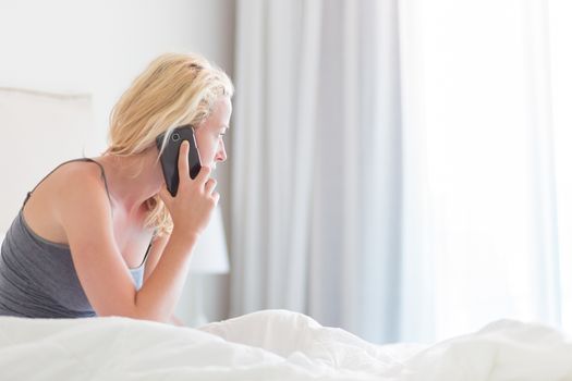 Portrait of  young lady with mobile phone in bed at home. Tired sleepy woman receiving emergency call in bed early in the morning.