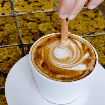 A coffee cup Latte being stirred by Cinnamon sticks.