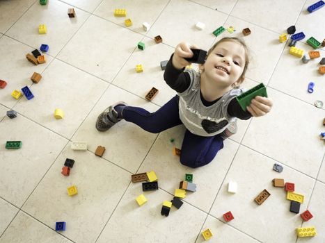 girl playing with colored bricks scattered on the floor