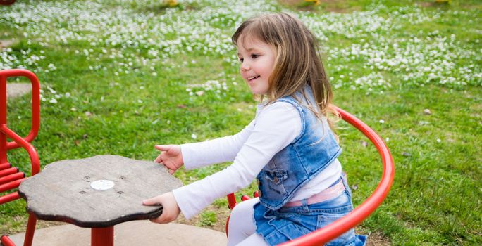 little girl turns into a manual carousel in an outdoor playground