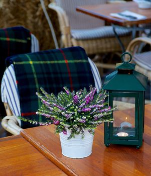 Elegant Rustic Sidewalk Cafe with Wooden Tables, Green Table Lamp, Flower Pot of Lavender and Checkered Plaid on Chair Outdoors