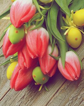 Bunch of Magenta Tulips with Yellow and Green Spotted Easter Eggs closeup on Wooden background. Retro Styled