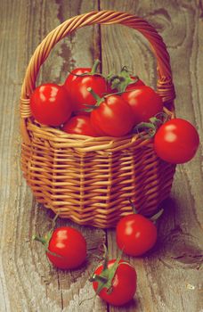 Perfect Ripe Cherry Tomatoes with Stems in Wicker Basket closeup on Rustic Wooden background. Retro Styled