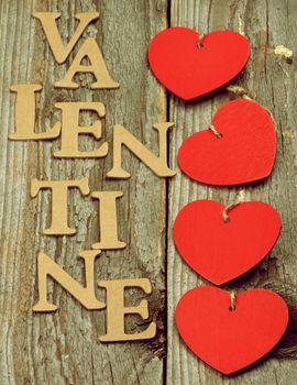 Arrangement of Four Red Hearts and Cardboard Words Valentine on Rustic Wooden background. Retro Styled