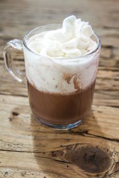 chocolate drink with whipped cream in transparent cup on rough wooden table