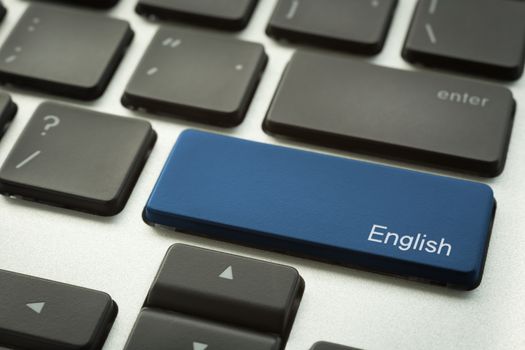 Close up laptop keyboard focus on a blue button with typographic word ENGLISH for education and language concepts.