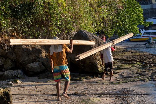 BALI, NUSA PENIDA ISLAND, INDONESIA - JULY 27.2015: Men transports cargo from ship to the shipyard in the hands. There is no other possibility to transport. Nusa Penida July 27. 2015 Indonesia