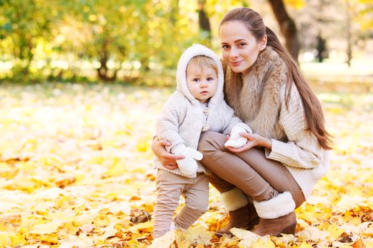 Mother and child having fun in autumn park among yellow leaves