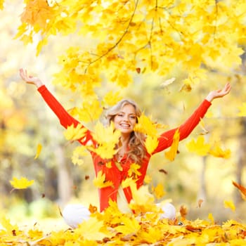 Happy woman throwing autumn leaves in the park