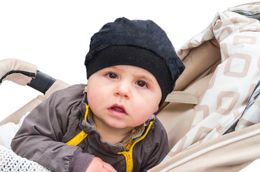 Baby with black cap sitting in a stroller, looking amazed. Background isolated.