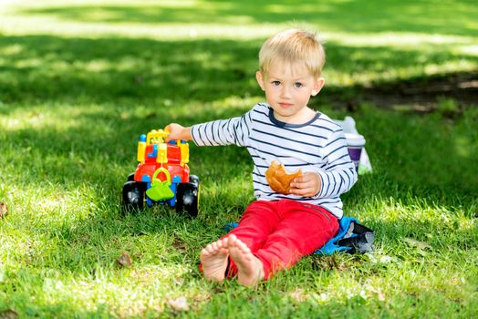 Little preschool boy playing with big toy car and having fun, outdoors.