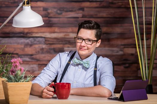 Smiling Dapper woman at stylish office desk with a red coffee mug