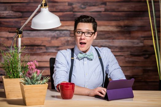 Surprised dapper woman wearing glasses and bowtie using tablet computer