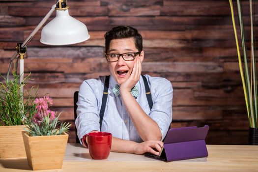 Happy dapper woman wearing glasses and bowtie with cup and tablet computer