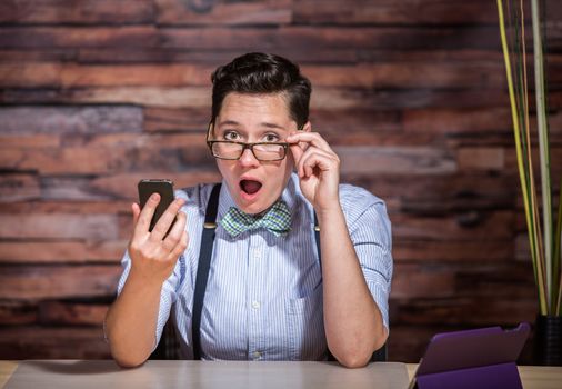 Surprised dapper woman in bowtie and eyeglasses looking at phone