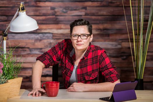 Woman in flannel shirt leaning on modern desk with red cup