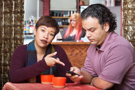 Annoyed woman pointing at cell phone held by man