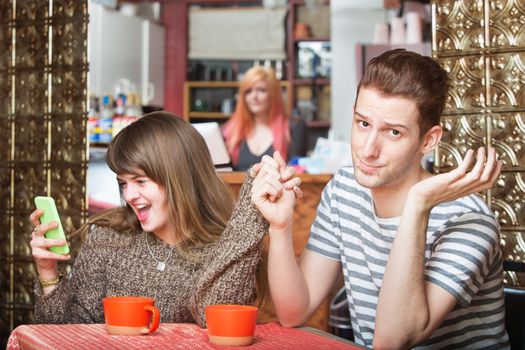 Young woman laughing and holding phone of embarrassed man