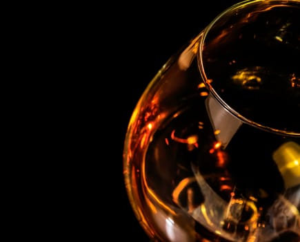 top of view of snifter of brandy in elegant typical cognac glass on black background with red reflection, with light tint red